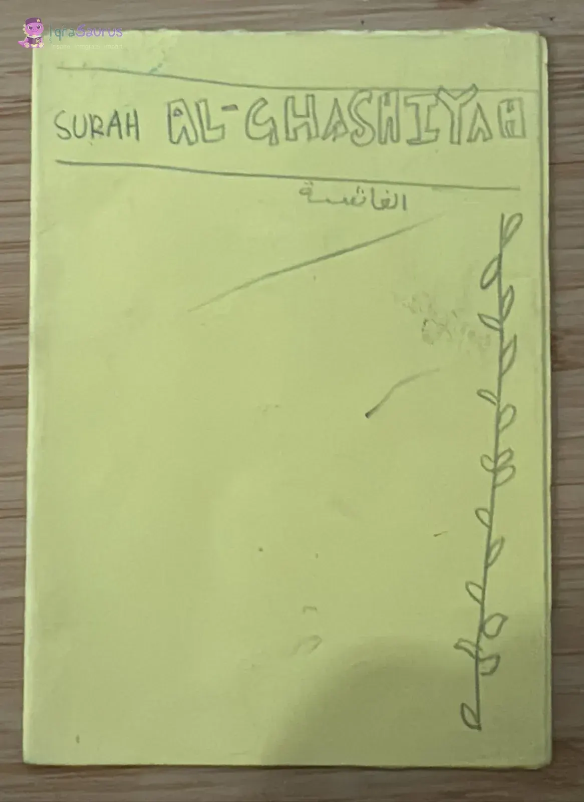 A yellow folded-paper cover with the surah name in outlined letters, the name written in Arabic below, and a climbing vine down one side.